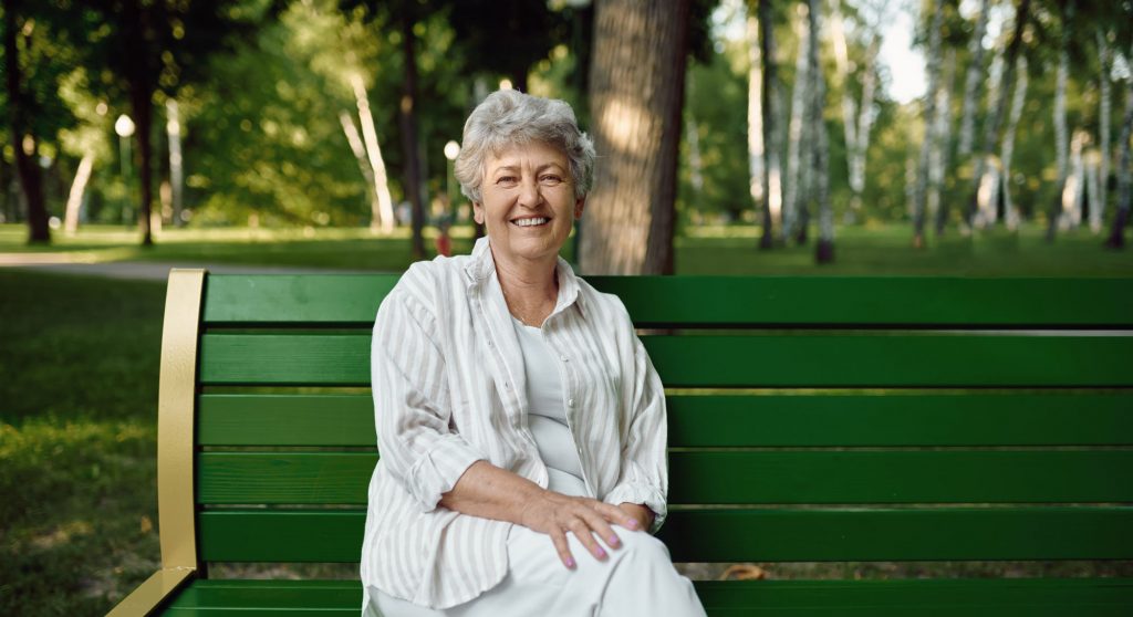 Happy Senior Woman Sitting on a Bench in the Park