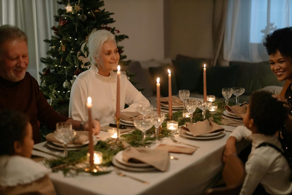 a family sits around a table set with Christmas decor and candles, smiling at each other