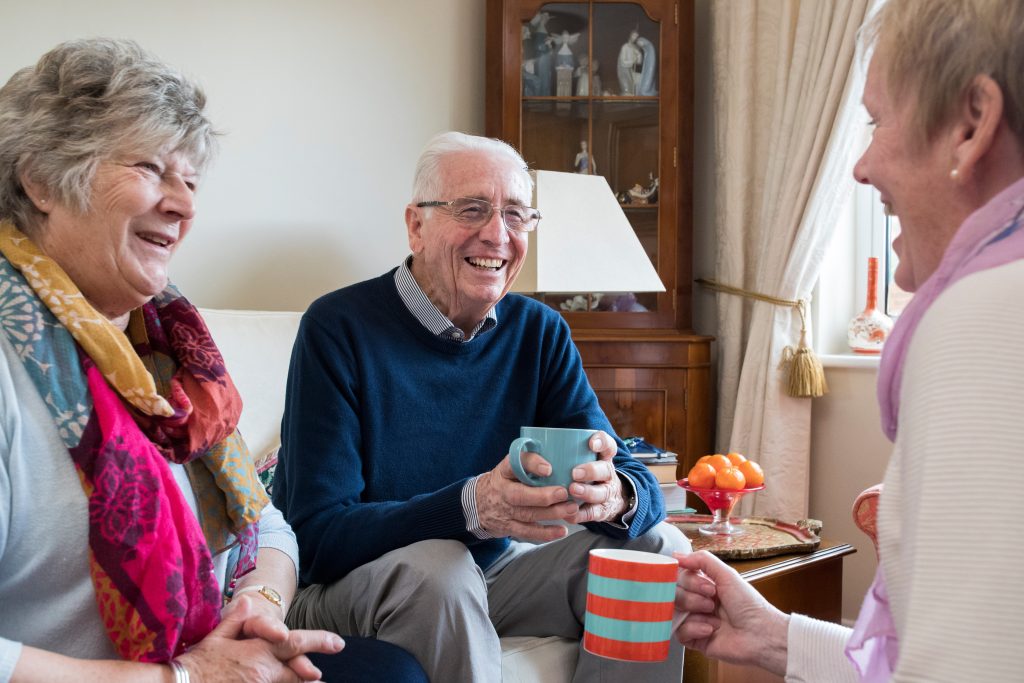 a group of seniors sit together drinking tea, smiling